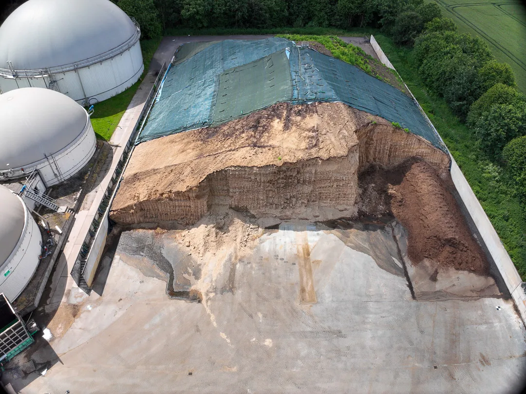 Senkrechte Luftaufnahme eines Fahrsilos mit angeschnittener Silage neben einer Biogasanlage